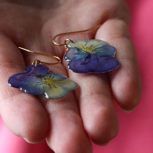 Real pansy flower earrings held in hand showing natural petal detail