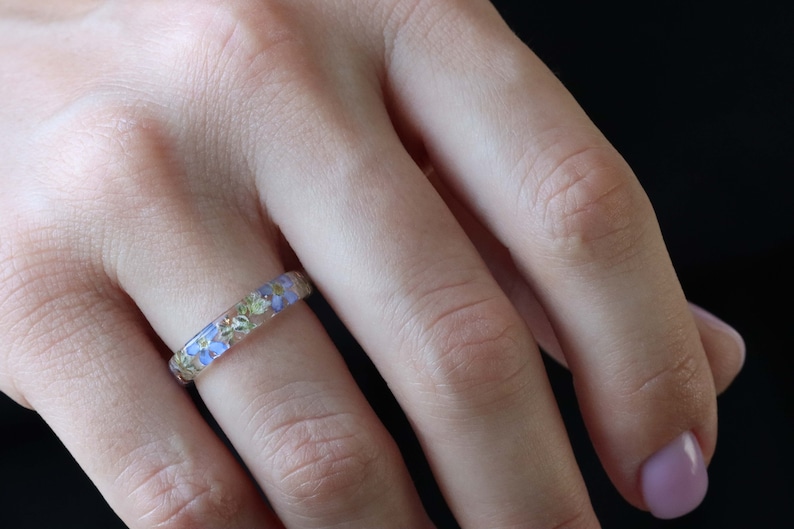 May include: A delicate ring with a band of clear resin embedded with tiny blue and green flowers.