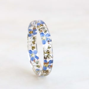 May include: A clear resin ring with blue forget-me-not flowers pressed inside.