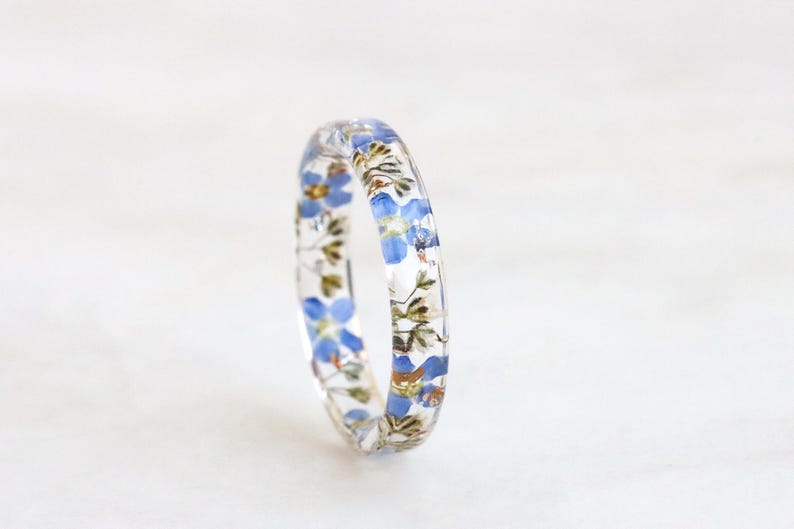 May include: A clear resin ring with blue forget-me-not flowers pressed inside.