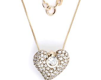 Puede incluir: Un collar de cadena de oro con un colgante en forma de corazón incrustado con pequeñas piedras transparentes. El colgante tiene una piedra transparente más grande en el centro.