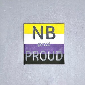 Może przedstawiać: Płótno w pasy żółte, białe i fioletowe z napisem "NB and PROUD" czarnymi literami.