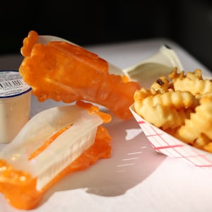 May include: A white plastic container of dipping sauce with a blue lid and a green label.  Two orange plastic containers with a clear plastic insert. A white paper container with red and white checkered pattern filled with golden brown crinkle-cut french fries.