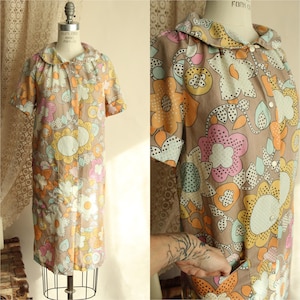 May include: A vintage dress with a floral pattern in brown, orange, pink, yellow, and blue. The dress has short sleeves, a rounded collar, and a button-down front. The dress is displayed on a mannequin.