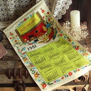May include: Vintage 1981 calendar towel with a green calendar grid and floral border. The towel features a colorful illustration of a home with the text "Bless Our Home". A vintage book and candle are also visible.