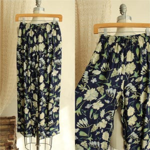 May include: Navy blue floral print pants with an elastic waistband. The pants feature a pattern of white and light green flowers and leaves. The pants are displayed on a mannequin.