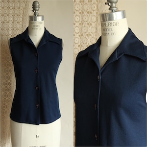 Op de afbeelding: Een mouwloos marineblauw overhemd met een kraag. Het overhemd wordt op een mannequin getoond. De knopen zijn donkerbruin van kleur. Het overhemd is gemaakt van een zacht materiaal.