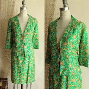 Puede incluir: Traje de falda verde vintage con blazer a juego. El traje presenta un vibrante estampado de cachemira verde con detalles en naranja y blanco. La chaqueta tiene mangas tres cuartos y cuello con solapas. La falda llega a la rodilla.