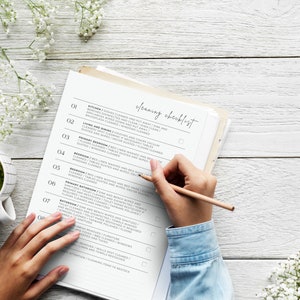 K&ouml;nnte beinhalten: Eine Reinigungscheckliste mit einer Hand, die einen Bleistift h&auml;lt und Punkte auf der Liste abhakt. Die Checkliste enth&auml;lt Aufgaben f&uuml;r K&uuml;che, Wohn- und Esszimmer, Hauptschlafzimmer, Schlafzimmer, zweites Badezimmer, Badezimmer und Waschk&uuml;che.