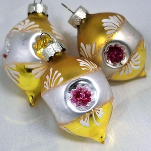 May include: Three vintage Christmas ornaments. Each ornament has a gold and silver color scheme with white accents. A pink, flower-shaped embellishment is centered on each ornament. The ornaments have a teardrop shape.
