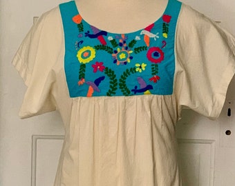May include: A white cotton dress with a blue embroidered yoke featuring colorful flowers and birds. The dress has short sleeves and a gathered waist.