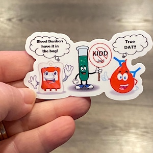 May include: Three cartoon characters representing blood donors. A red blood bag with a smiling face, a green test tube with a smiling face holding a sign that says "KIDD-ing!" and a red blood cell with a smiling face and a speech bubble that says "True DAT!!".