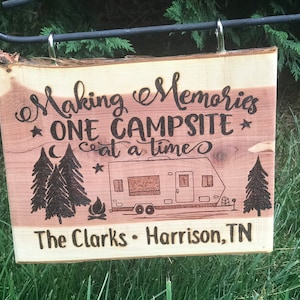 May include: Wooden sign with the text "Making Memories *ONE CAMPSITE* at a time" and a drawing of a camper, trees, and a campfire. The sign also says "The Clarks - Harrison, TN".