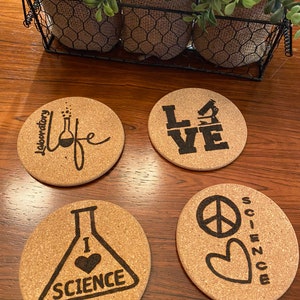 May include: Four round cork coasters with different designs. The first coaster has the text "Laboratory Life" with a beaker and bubbles. The second coaster has the text "LOVE". The third coaster has a beaker with a heart and the text "I love science". The fourth coaster has a peace sign, a heart, and the text "Science".