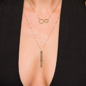 May include: A gold necklace with an infinity symbol charm and a long, thin pendant with Hebrew lettering.