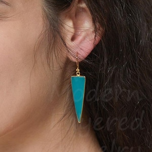 May include: A gold-toned earring featuring a long, downward-pointing triangular pendant with a smooth, vibrant turquoise-colored inlay. The earring hangs from a simple gold-toned hook wire, creating a sleek, geometric drop design that rests against the side of the face.