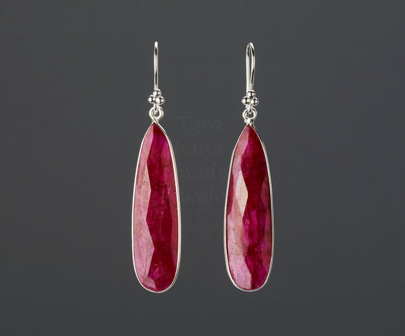以下が含まれることがあります： 涙型のルビーの宝石が付いた、シルバーのドロップイヤリングのペア。イヤリングはシンプルなデザインで、普段使いに最適です。