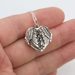 May include: A silver heart-shaped locket pendant with detailed wing designs. The locket opens to reveal space for a small photo or keepsake. The pendant hangs from a delicate silver chain, creating a sentimental piece of jewellery.