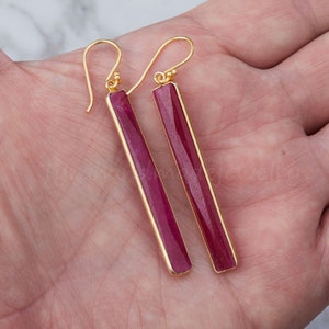 May include: A pair of gold earrings with long, rectangular, red gemstone drops.