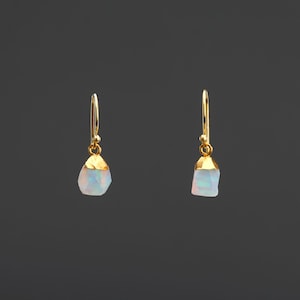 Könnte beinhalten: Ein Paar goldene Ohrringe mit einem weißen Opal-Stein an jedem Ohrring.