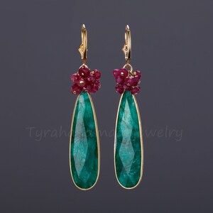 May include: Gold earrings with a teardrop-shaped emerald green gemstone and a cluster of ruby red stones.