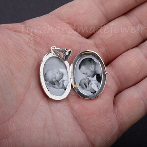 May include: Open silver oval locket with two black and white photos inside. The locket is open, revealing a photo of a baby and a photo of a person kissing a baby. The locket is held in a hand.