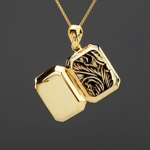 Könnte beinhalten: Eine goldene Halskette mit einem Anhänger in Form eines Medaillons, der auf der Vorderseite mit einem detaillierten Blumenmuster verziert ist. Das Medaillon ist geöffnet und zeigt ein leeres Inneres.