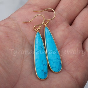 May include: A pair of gold dangle earrings with turquoise teardrop-shaped stones. The earrings have a simple design and are perfect for everyday wear.