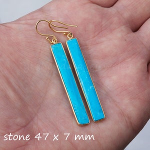 May include: A pair of long, rectangular drop earrings featuring bright turquoise stones set in gold-toned metal frames with hook-style ear wires. The stones measure 47 mm by 7 mm, as indicated by the text printed at the bottom of the image.