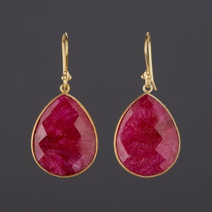 May include: A pair of gold earrings with teardrop-shaped red gemstone pendants.