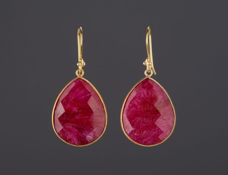 May include: A pair of gold earrings with teardrop-shaped red gemstone pendants.