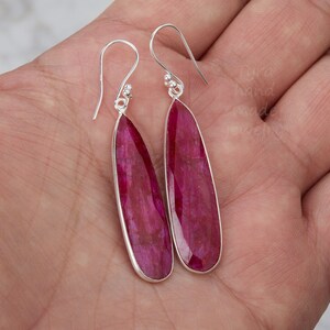 以下が含まれることがあります： 長いしずく型のルビーの宝石が付いた、銀製のドロップイヤリングのペアです。