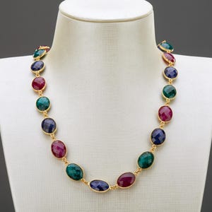 Può includere: Una collana d'oro con pietre ovali in tonalità di verde, blu e rosso.