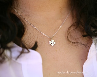 May include: A silver necklace with a four-leaf clover pendant. The necklace is on a model wearing a white shirt.