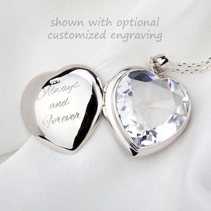 Op de afbeelding: Een zilveren hartvormig medaillon met een heldere kristallen bovenkant. Het medaillon is open en de binnenkant is gegraveerd met de woorden "Always and Forever".