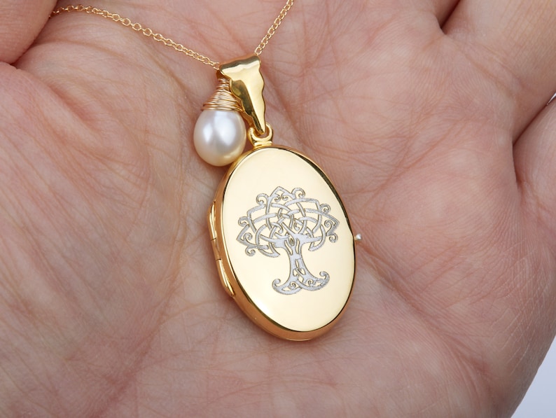 May include: Gold-tone oval locket necklace with a Celtic tree design. A small white pearl hangs from the chain. The locket is approximately 1 inch in length and is suspended from a delicate gold chain.
