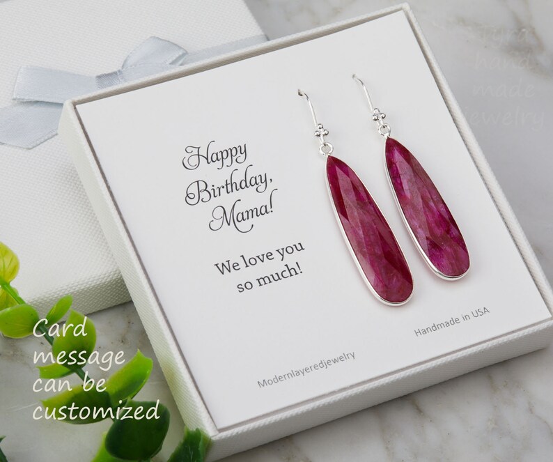 以下が含まれることがあります： 白いギフトボックスには、「ハッピーバースデー、ママ！愛してるよ！」と書かれたカードが入っています。ボックスには、ピンクの宝石の雫が付いたシルバーのドロップイヤリングのペアが入っています。カードのメッセージはカスタマイズできます。アメリカ製です。