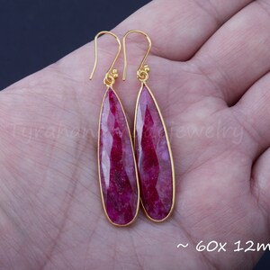 以下が含まれることがあります： 涙型のピンクのルビーの石が付いた、ゴールドのイヤリングのペア。イヤリングは約60x12mmです。