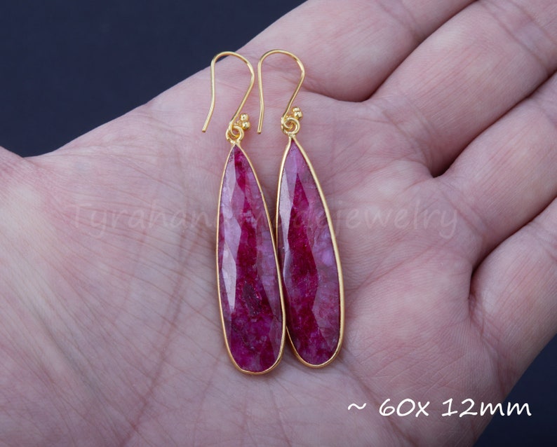 以下が含まれることがあります： 涙型のピンクのルビーの石が付いた、ゴールドのイヤリングのペア。イヤリングは約60x12mmです。