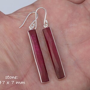 May include: A pair of silver earrings with long, rectangular, dark red gemstone drops. The stone measures 47 x 7 mm.