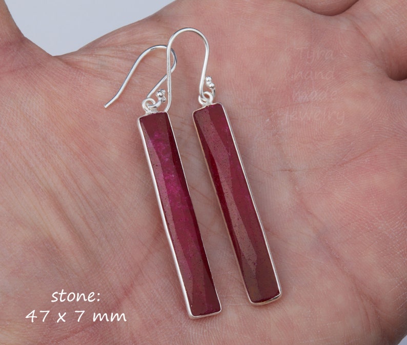May include: A pair of silver earrings with long, rectangular, dark red gemstone drops. The stone measures 47 x 7 mm.