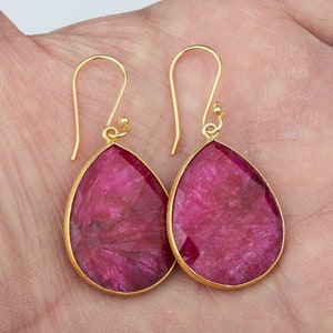 May include: A pair of gold earrings with pink teardrop-shaped gemstones. The earrings have a simple design and are perfect for everyday wear.