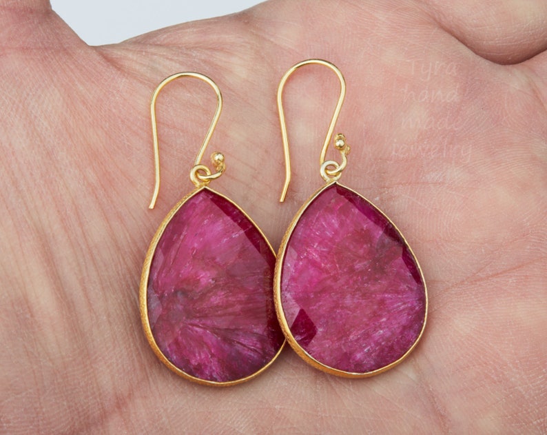 May include: A pair of gold earrings with pink teardrop-shaped gemstones. The earrings have a simple design and are perfect for everyday wear.