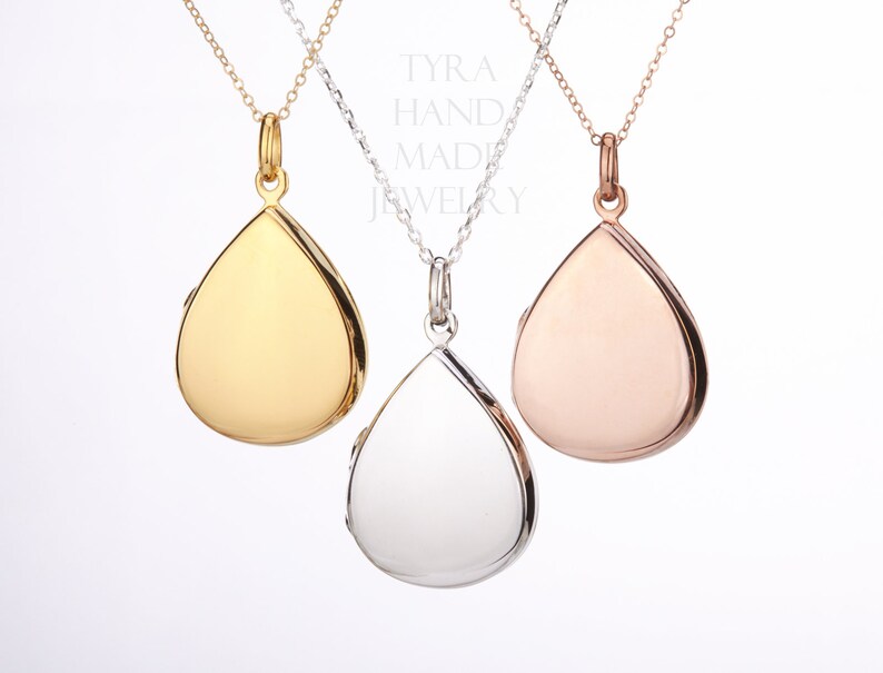 May include: Three teardrop-shaped locket necklaces in gold, silver, and rose gold. The lockets are hanging from delicate chains.