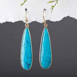 May include: A pair of teardrop-shaped turquoise earrings with gold-toned metal settings.