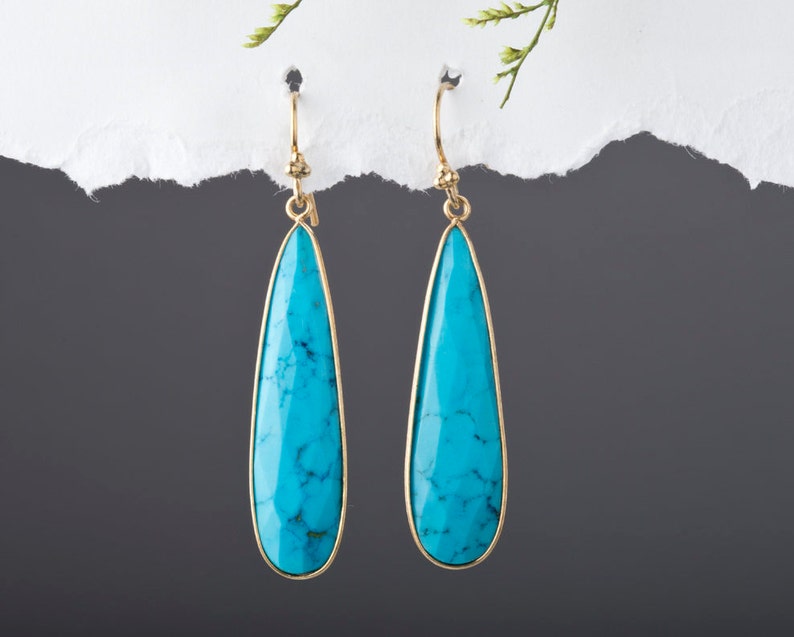 May include: A pair of teardrop-shaped turquoise earrings with gold-toned metal settings.