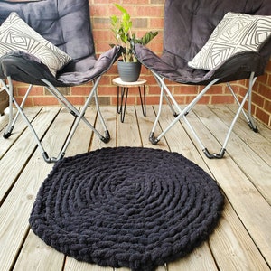 May include: Black round braided rug on a wooden deck with two black folding chairs and a small potted plant on a metal stand.