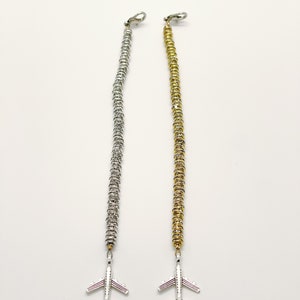 May include: Two beaded lanyards, one with silver-toned beads and one with gold-toned beads, each featuring a silver-toned airplane charm at the bottom and a lobster claw clasp at the top. The beads are small, round, and stacked in a long vertical line.