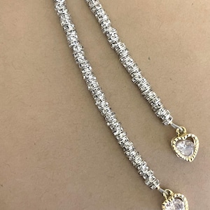 May include: Two silver-colored, rhinestone-studded strands with gold-toned heart-shaped pendants. The strands are composed of small, round rhinestones, and the pendants have a clear, heart-shaped stone in the center.