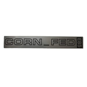 May include: A silver metal sticker with the text "CORN_FED" and the number "E885" printed in black.